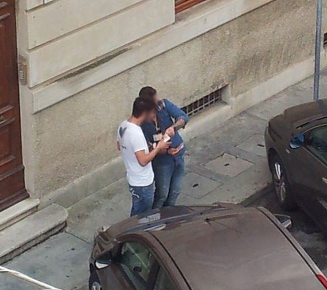 L'uomo con giacca e pantaloni di jeans si fa consegnare i soldi da un passante, impietosito dalla storia che gli ha raccontato